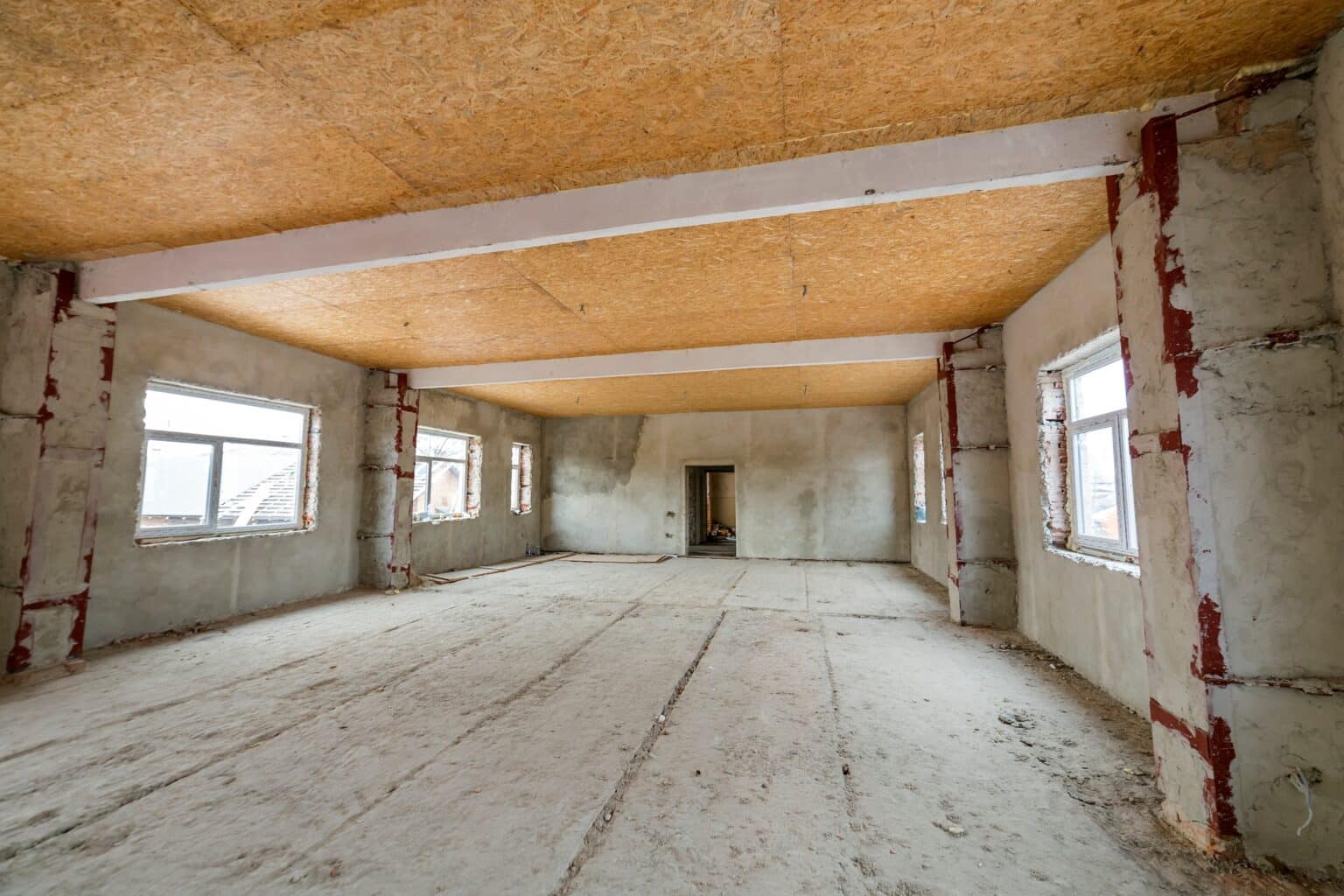 Unfinished apartment or house big loft room under reconstruction. Plywood ceiling, plastered walls, window openings, cement floor. Construction and renovation concept.